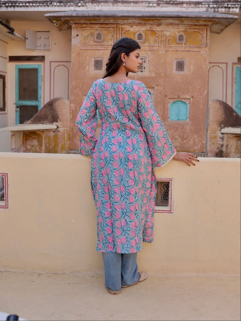 Woman in a floral dress standing on a balcony with a traditional building in the background