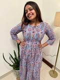 A woman smiling and posing in a traditional Alizeh kameez with handcrafted prints, standing indoors.